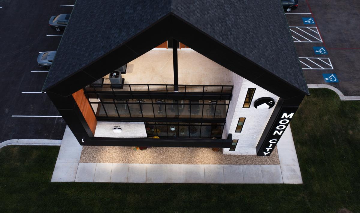 Top-down drone view of the gabled entrance canopy, glass front and parking at dusk