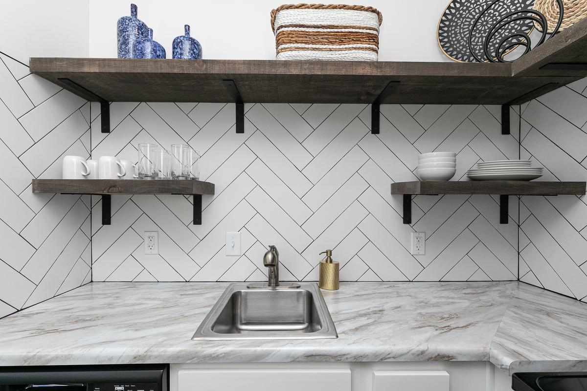 Kitchen detail: open wood shelves with dishes, herringbone tile backsplash, marble-look counter, sink