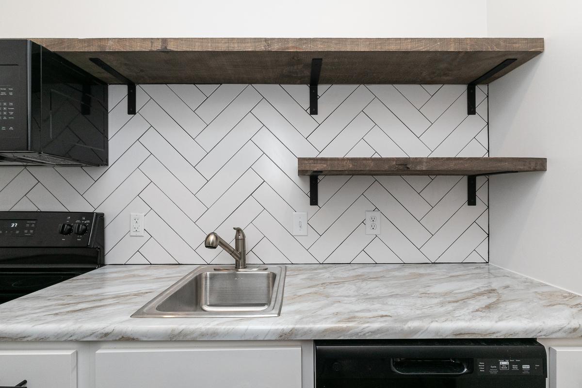 Vacant kitchen detail: sink, herringbone backsplash, open shelves, black microwave and range
