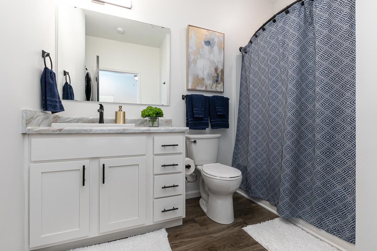 Bathroom: white vanity, marble-look top, navy patterned shower curtain, framed art