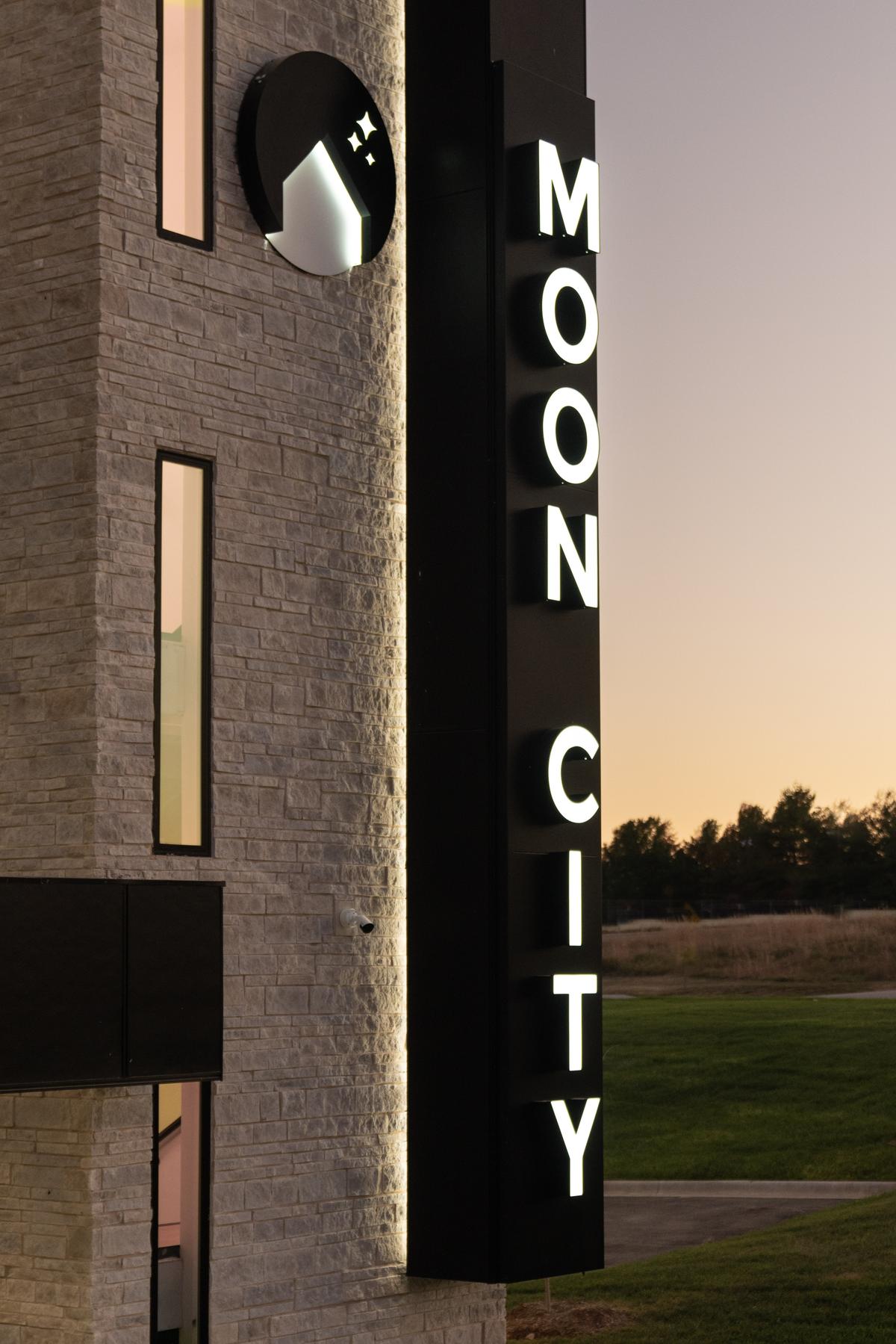 Vertical MOON CITY sign on the stone-clad corner at dusk