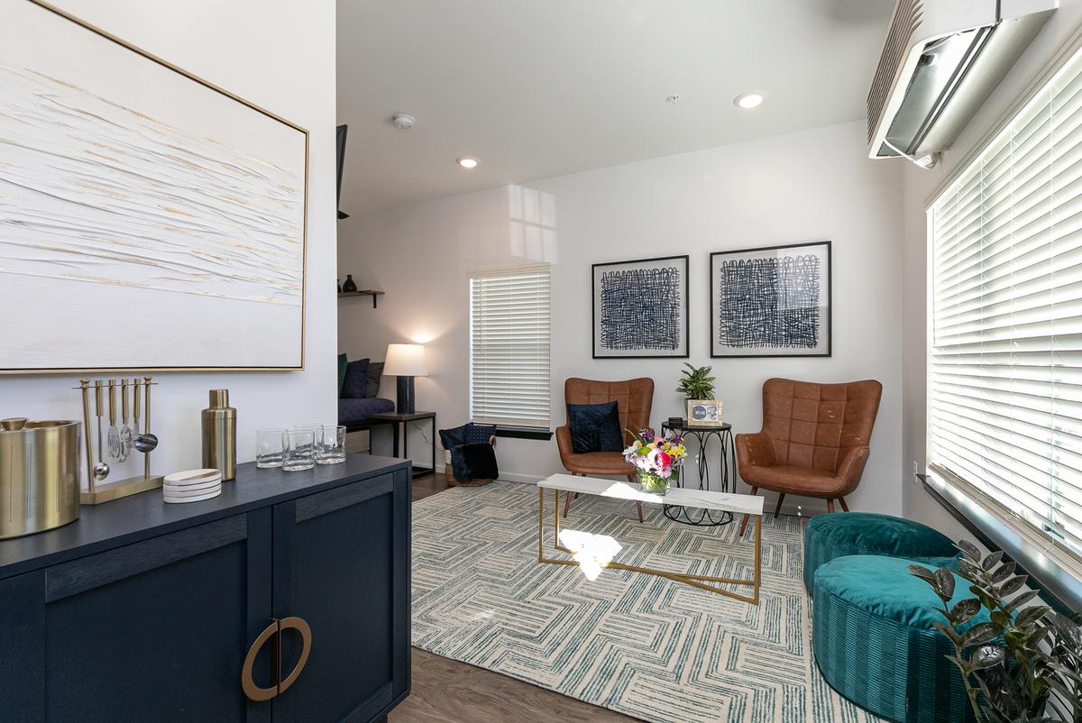 Living room from the kitchen: navy sideboard, wall art, tan chairs and teal ottomans
