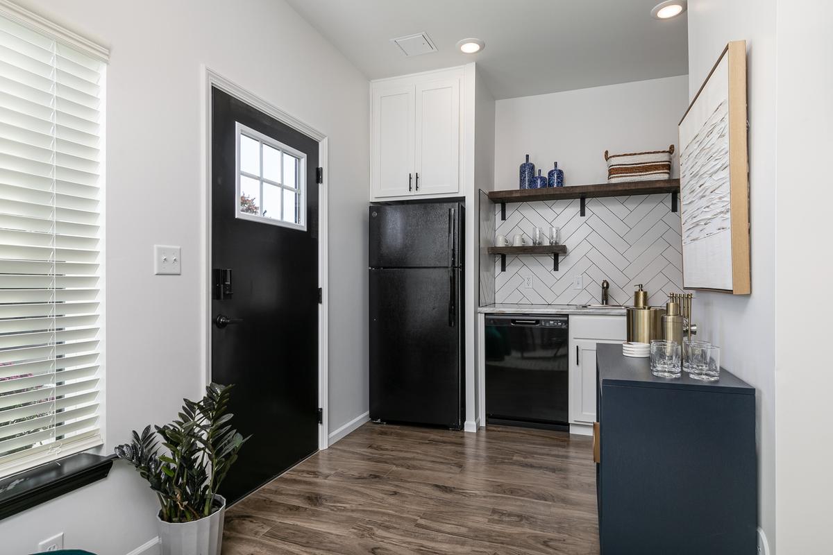 Entry with black front door, black refrigerator and dishwasher, open wood shelving on herringbone tile