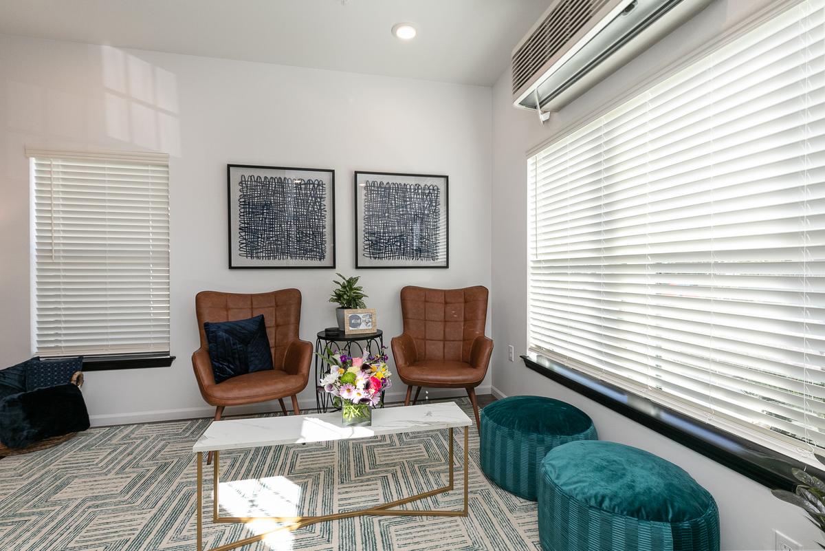 Living room by the window: two tan leather chairs, marble coffee table, teal ottomans, three framed prints
